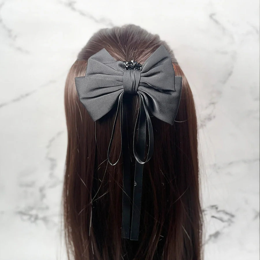 Black satin ribbon bow clips attached to long brown hair with decorative beads and hanging ribbons