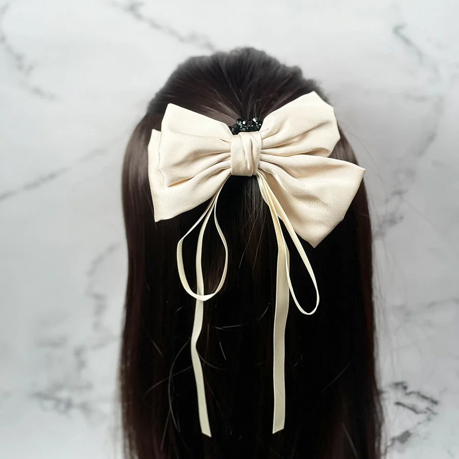 Cream satin ribbon bow clips attached to dark brown hair with flowing tail ribbons