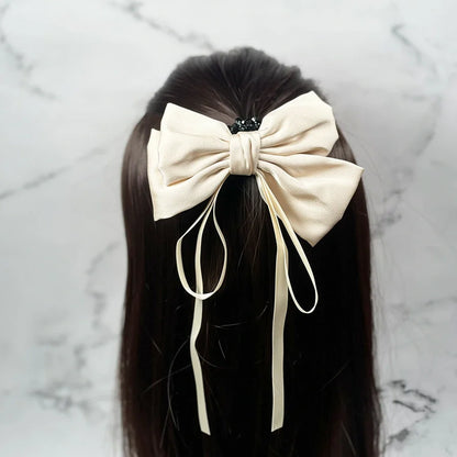 Cream satin ribbon bow clips attached to dark brown hair with flowing tail ribbons