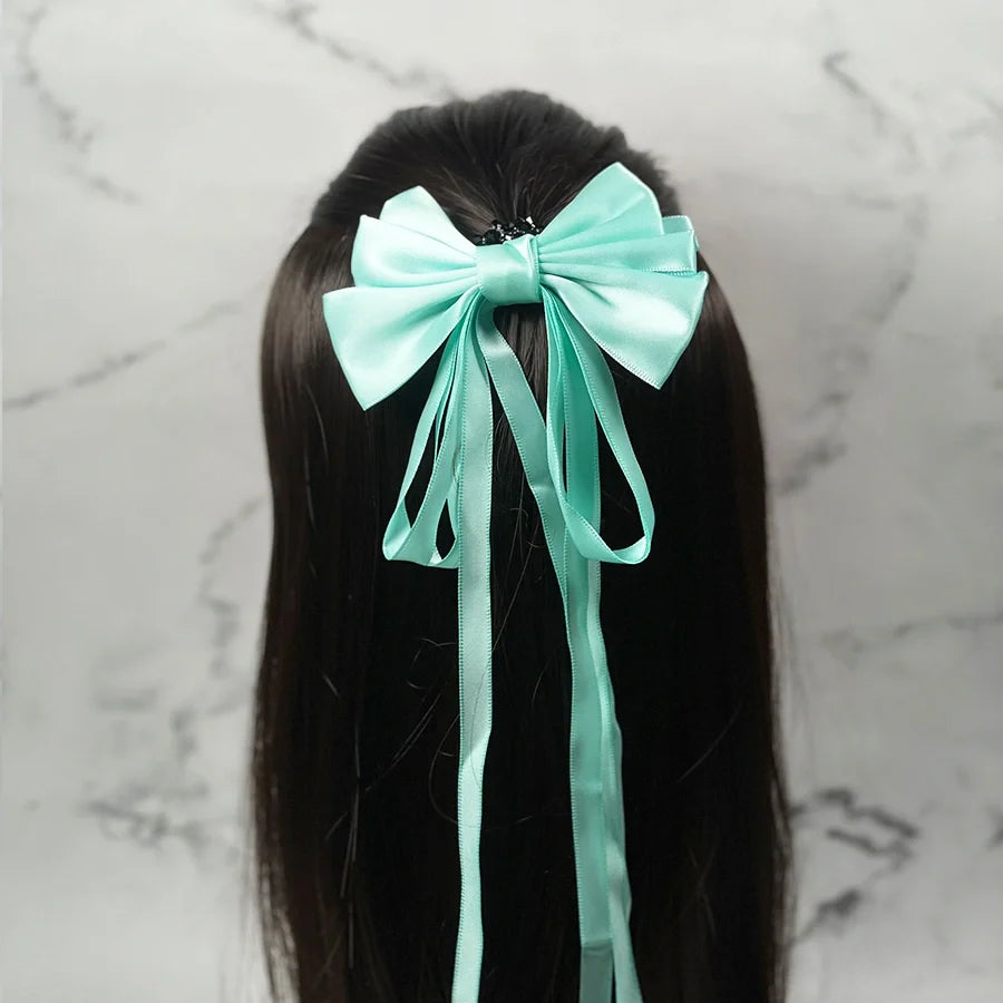 Mint green satin ribbon bow clips attached to long dark hair on a marble background