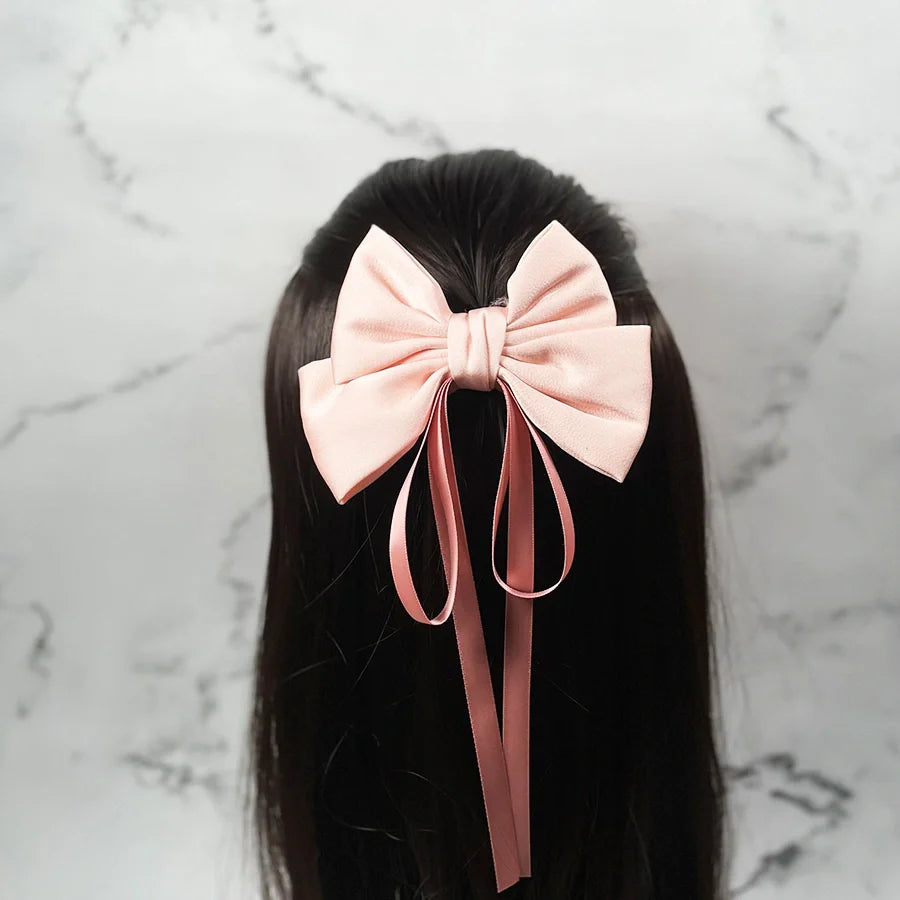 Pink satin ribbon bow clips worn on dark hair with long trailing ribbons against marble background