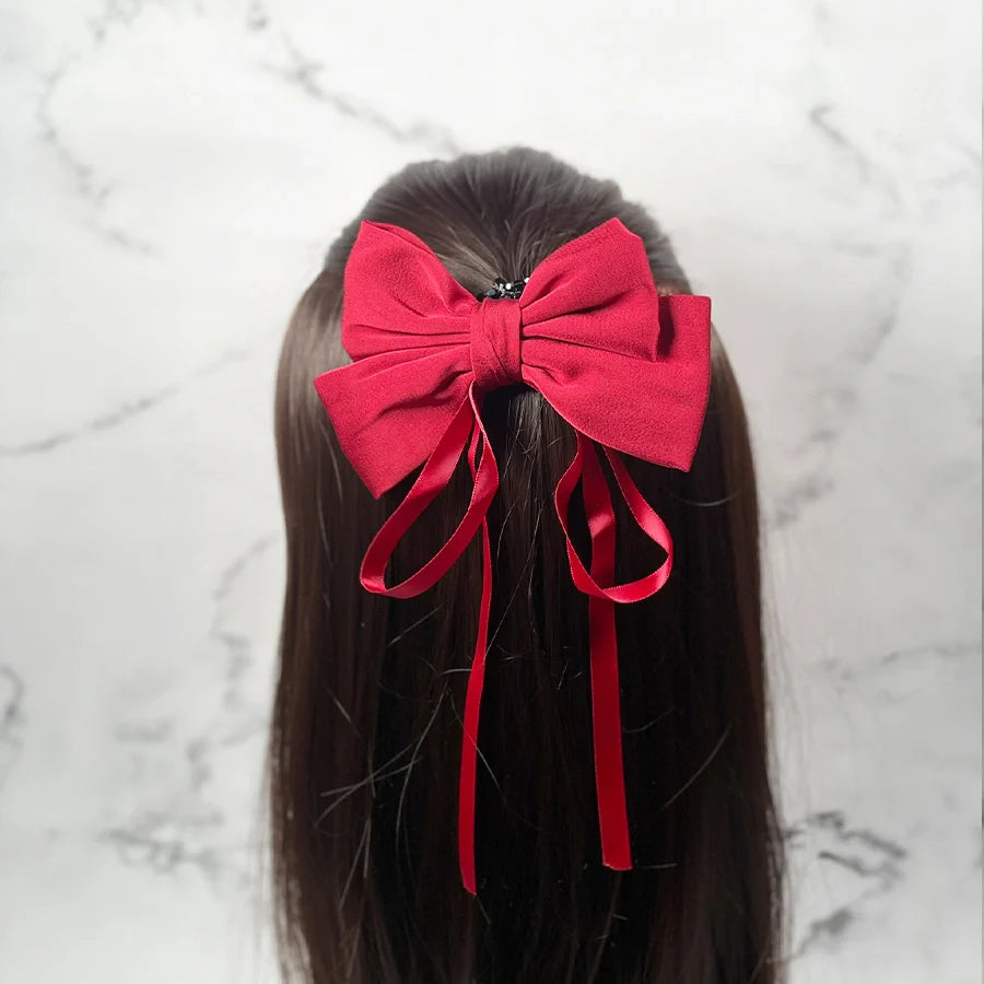 Red satin ribbon bow clips attached to long brown hair with flowing tails