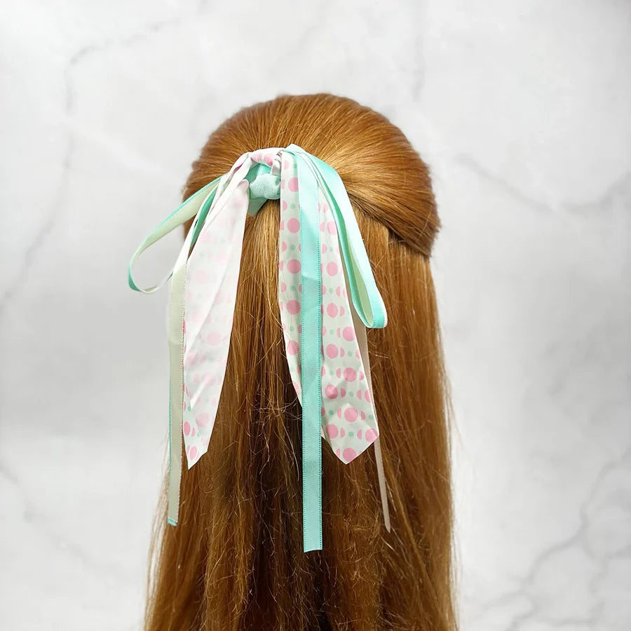 Scrunchies with ribbon for women in pastel colors tied on long brown hair against marble background