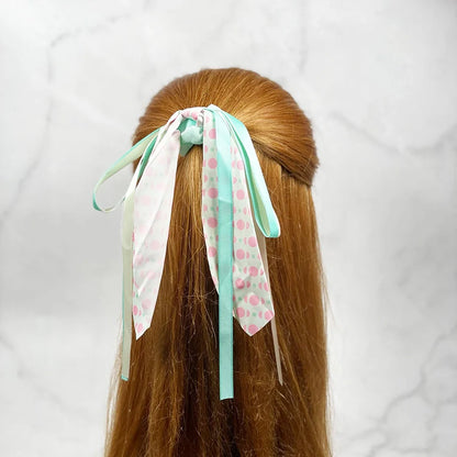 Scrunchies with ribbon for women in pastel colors tied on long brown hair against marble background