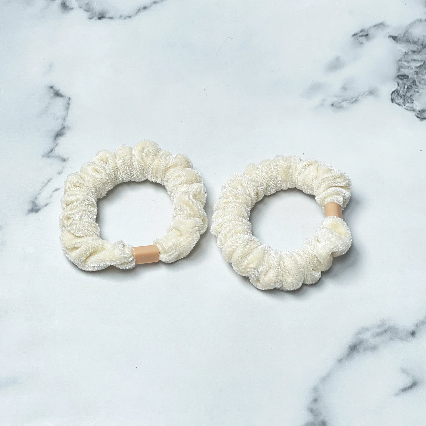 Two white shiny velvet hair ties with elastic stretch bands on marble surface