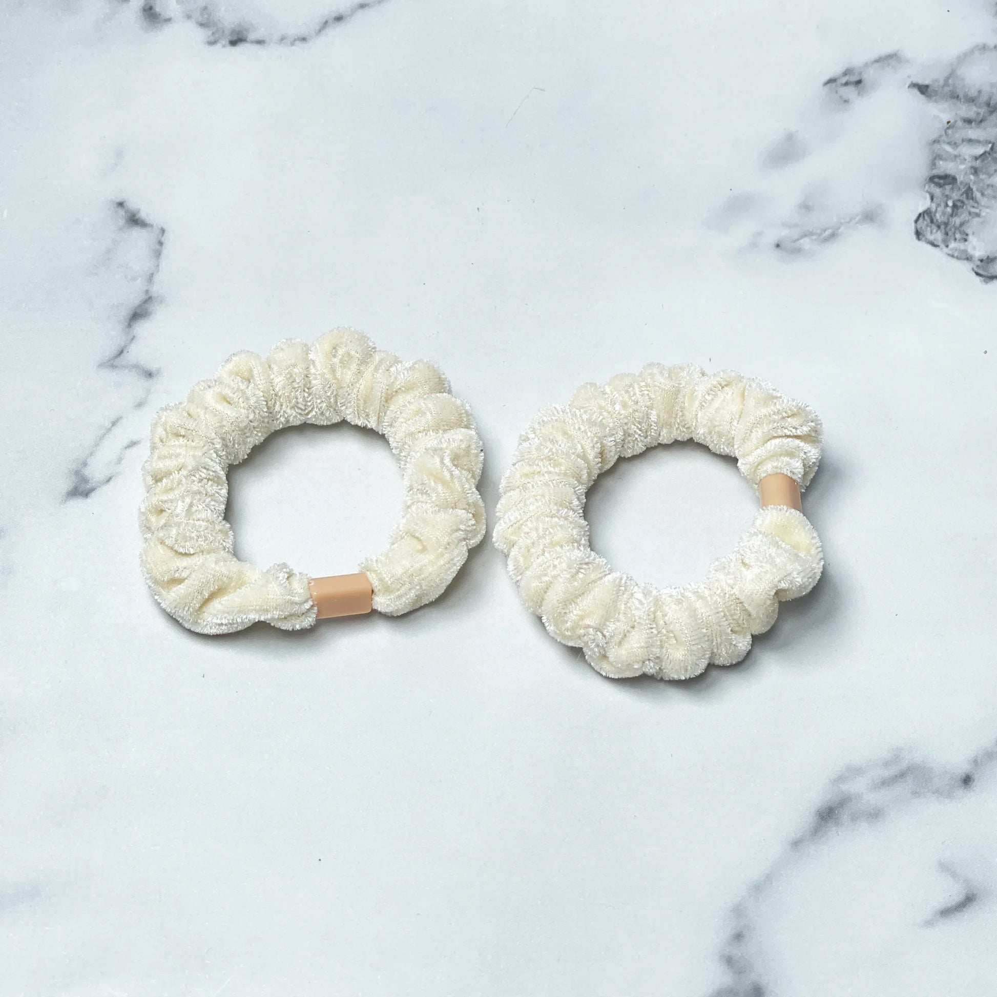 Two white shiny velvet hair ties with elastic stretch bands on marble surface