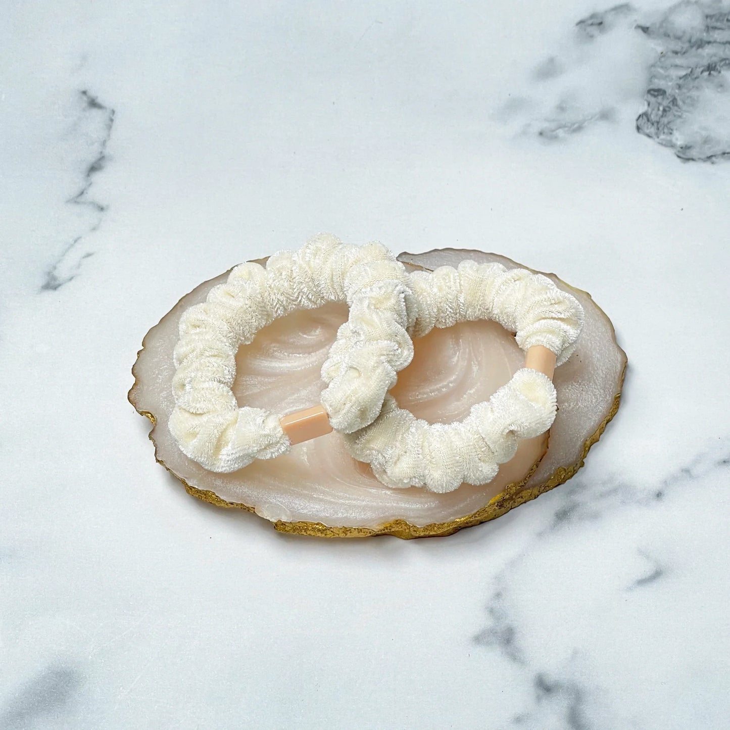 Cream color shiny velvet hair ties displayed on a decorative stone tray on marble surface