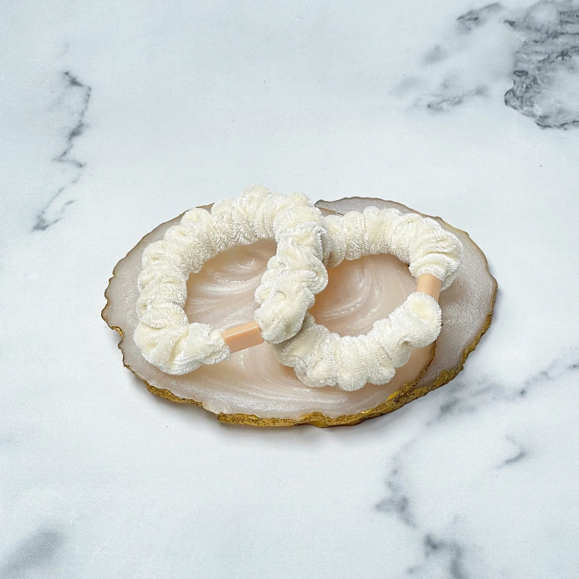Cream color shiny velvet hair ties displayed on a decorative stone tray on marble surface