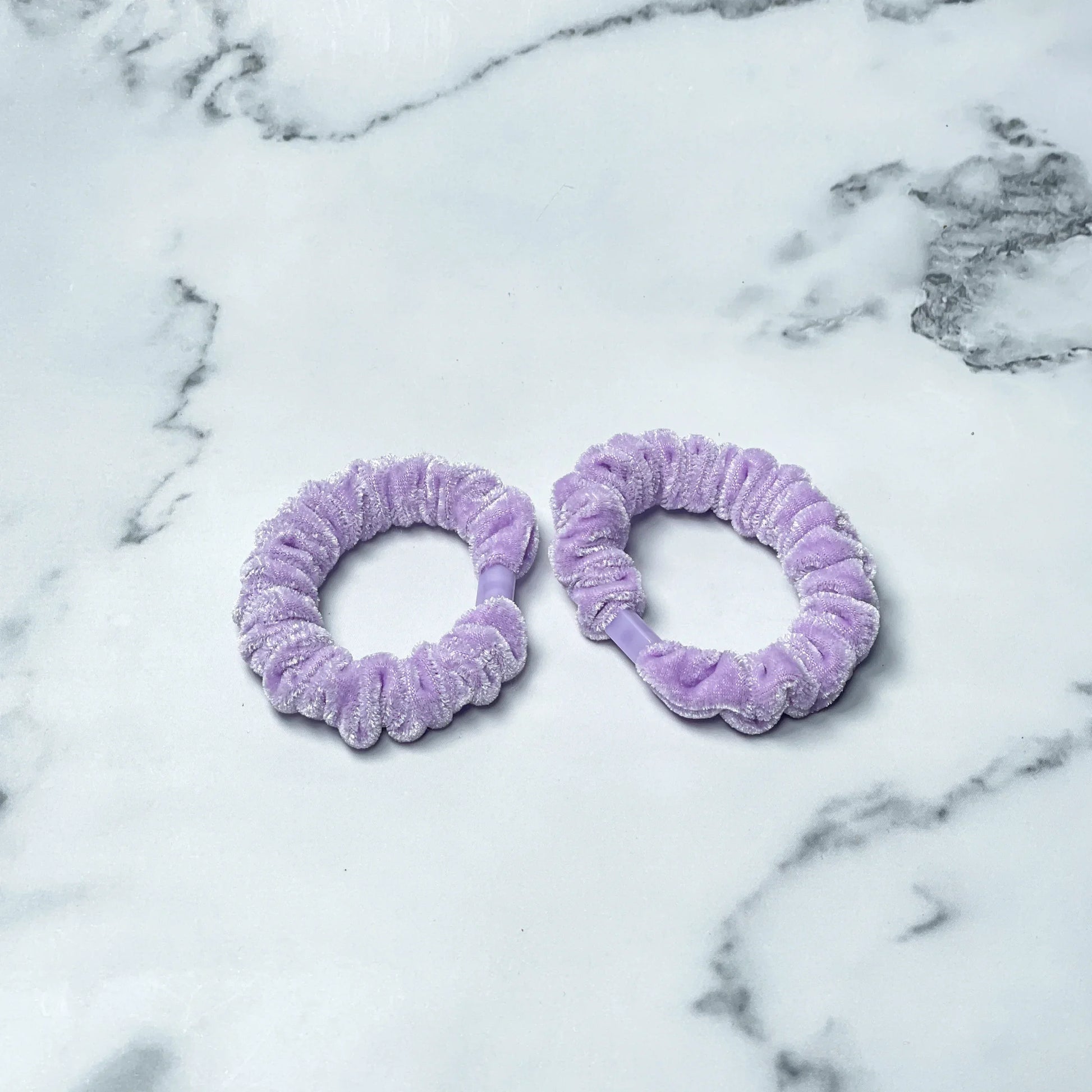 Two light purple shiny velvet hair ties on white marble surface from mydevelopmentstor