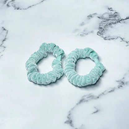 Two light blue shiny velvet hair ties on a white marble surface