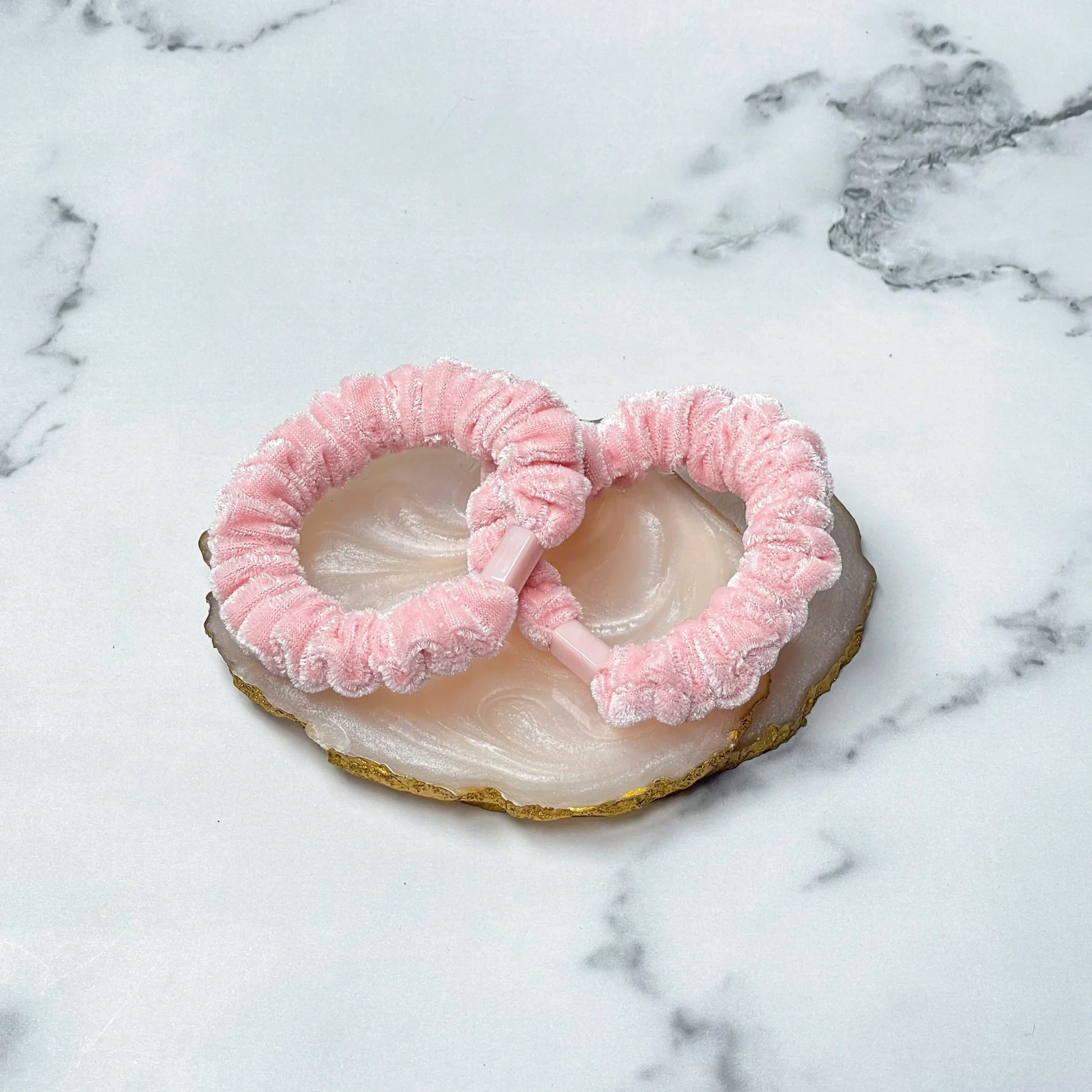 Pair of pink shiny velvet hair ties placed on a polished agate coaster on marble surface