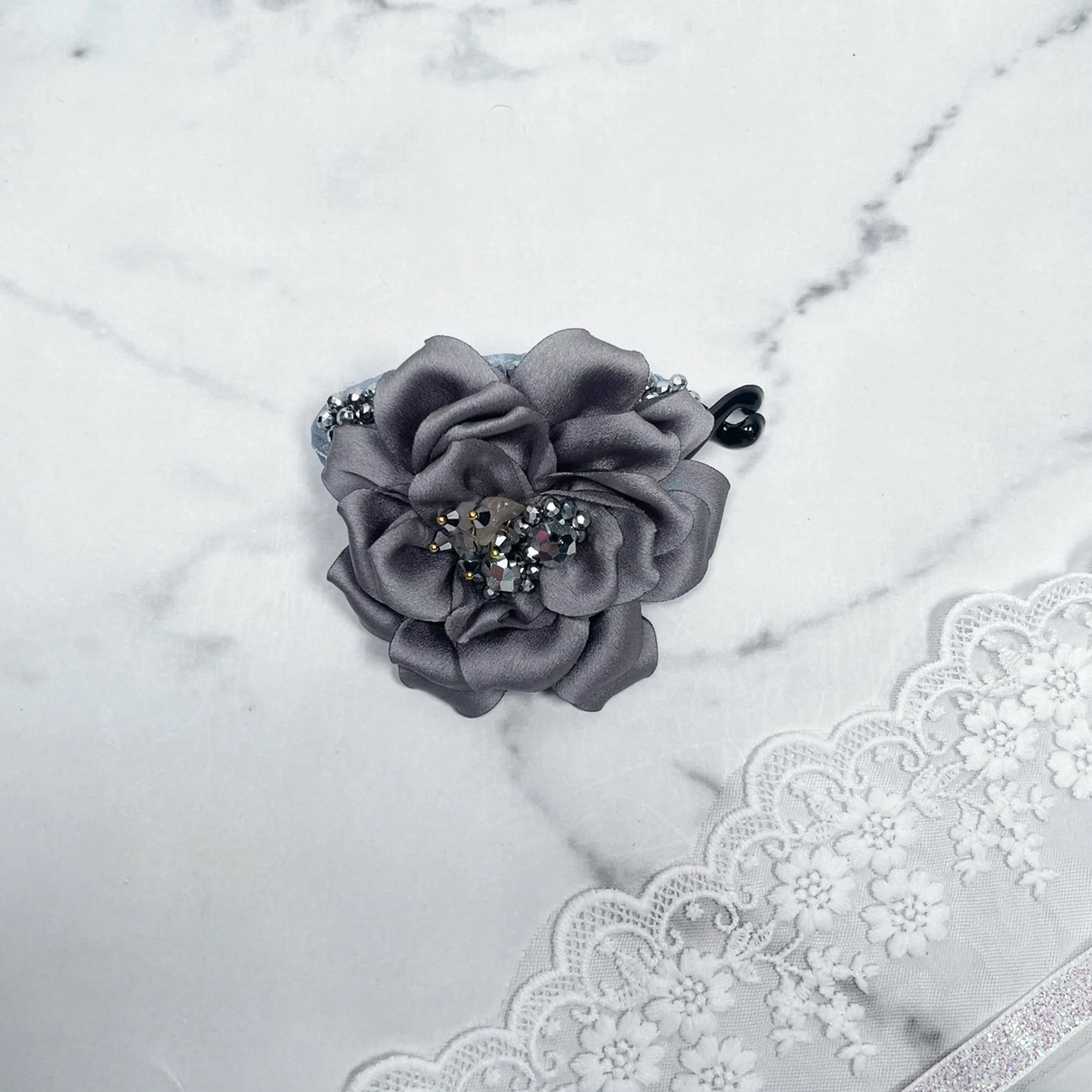 Bella Luxe silver crystal banana clip with gray fabric flower and decorative crystals on marble background