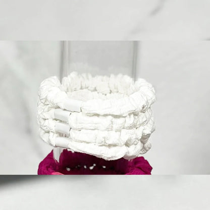 Set of white soft cloth hair ties stacked on a clear glass container with a magenta hair tie below