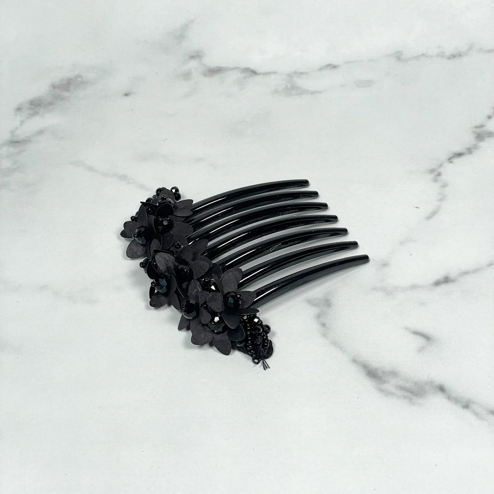Black studded hair bun comb with floral and bead embellishments on marble surface