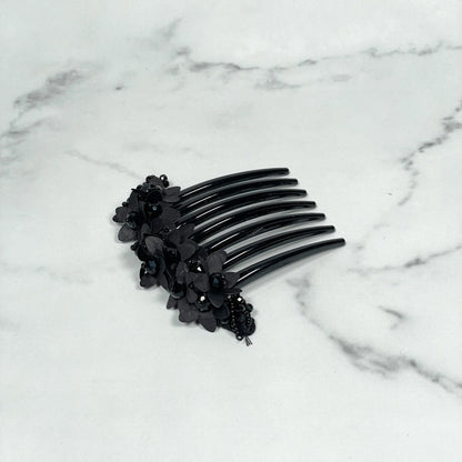 Black studded hair bun comb with floral and bead embellishments on marble surface