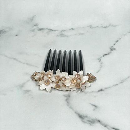 Black studded hair bun comb with white flower decorations and clear gem accents on marble background