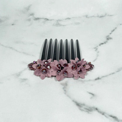 Black studded hair bun comb decorated with pink flowers and rhinestones on marble surface