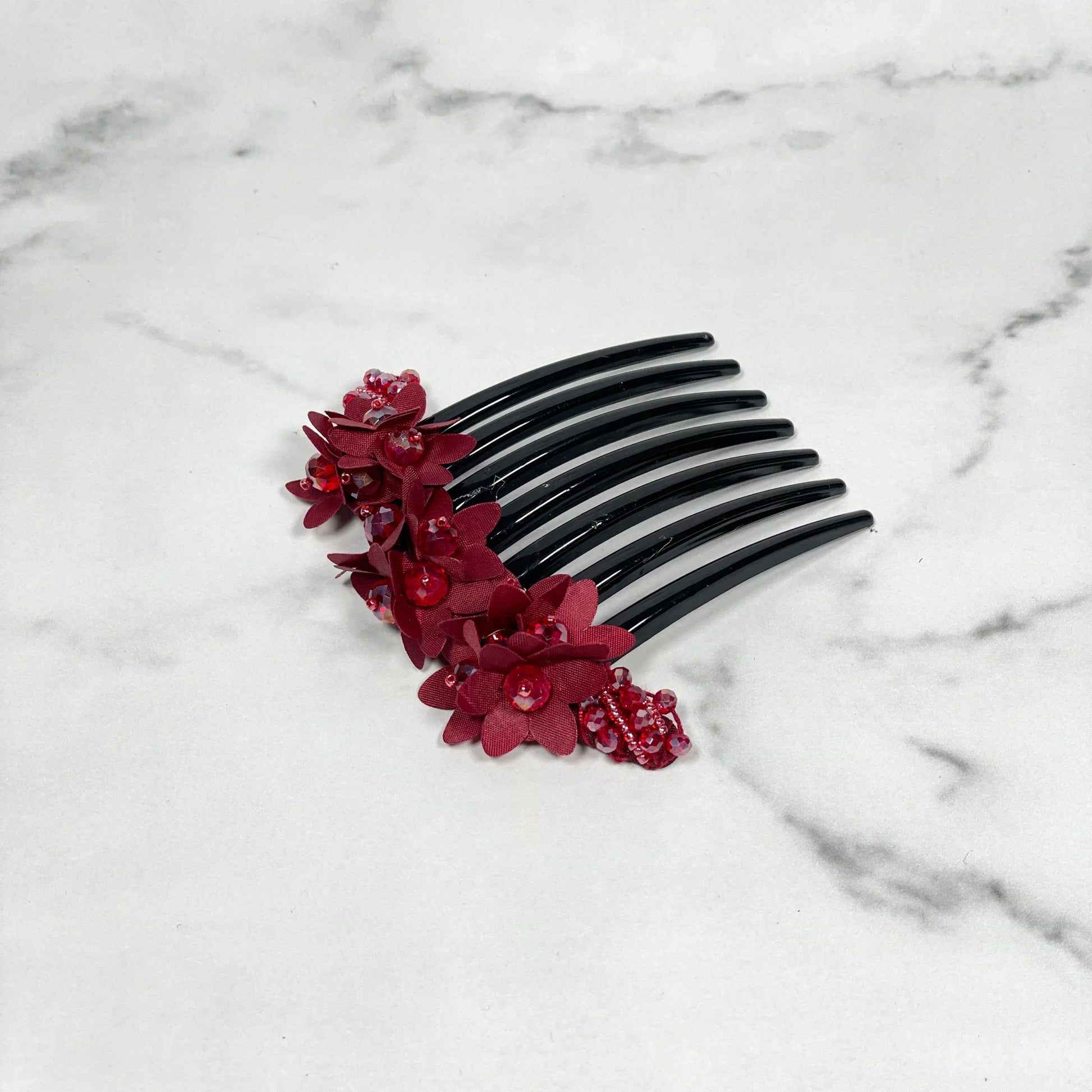 Black studded hair bun comb with red floral decorations on a white marble surface