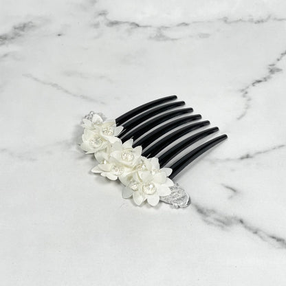 Black studded hair bun comb with white floral decorations and clear crystal accents on marble surface