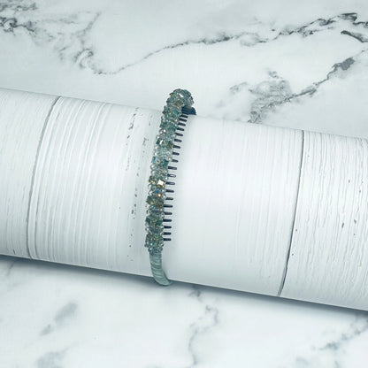 Studded headbands with green and clear crystals on a white textured cylindrical display