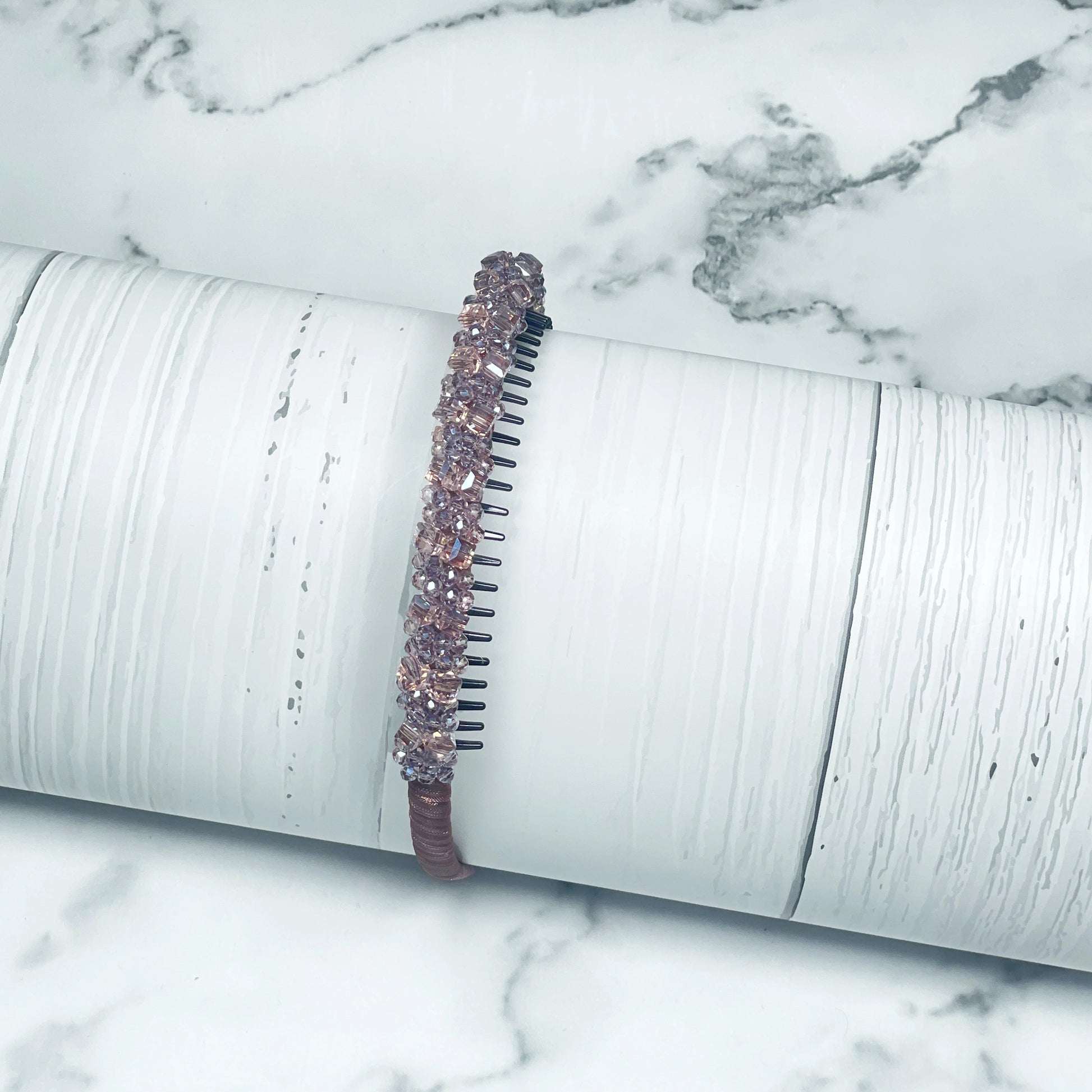 Brown studded headbands with sparkling rhinestones displayed on a white textured cylindrical stand
