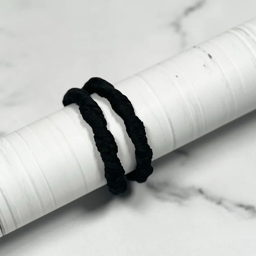 Black Thick Hair Ties wrapped around a white cylindrical object on marble surface