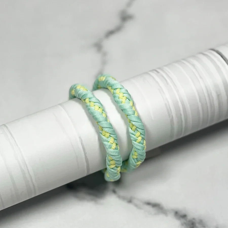 Light blue and yellow braided Thick Hair Ties shown wrapped around a white cylindrical object