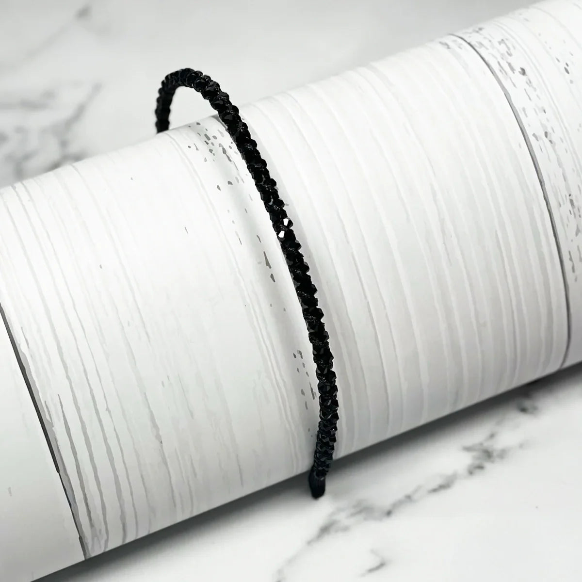 Black thin embellished headbands for women displayed on a white textured cylindrical stand