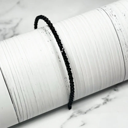 Black thin embellished headbands for women displayed on a white textured cylindrical stand