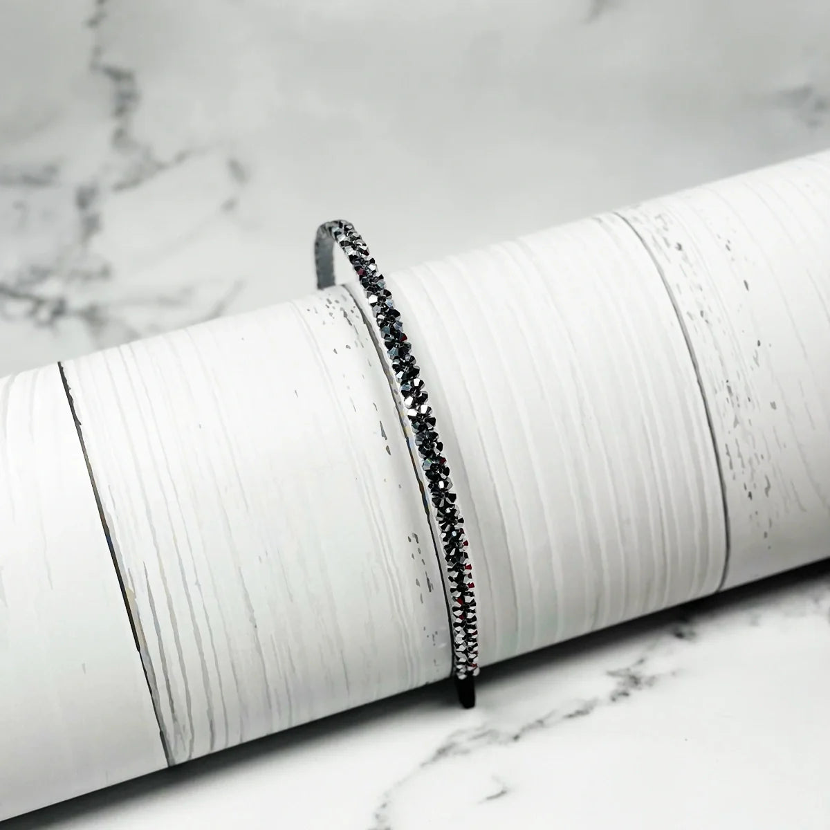 Black thin embellished headbands for women with sparkling stones on white textured background