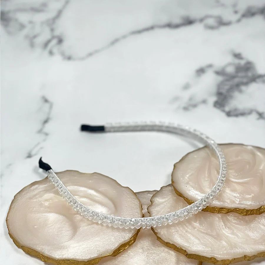 Clear thin embellished headbands for women displayed on white and gold decorative stones