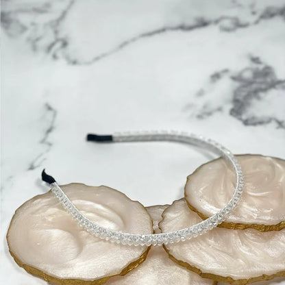 Clear thin embellished headbands for women displayed on white and gold decorative stones