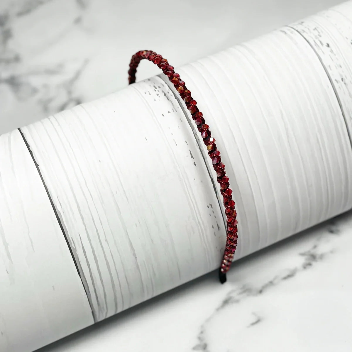 Red thin embellished headbands for women with sparkling stones displayed on white textured surface
