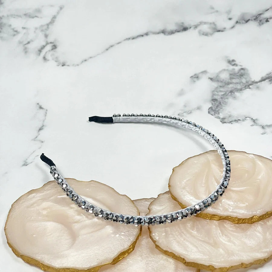 Silver thin embellished headbands for women displayed on white marble and beige stone coasters