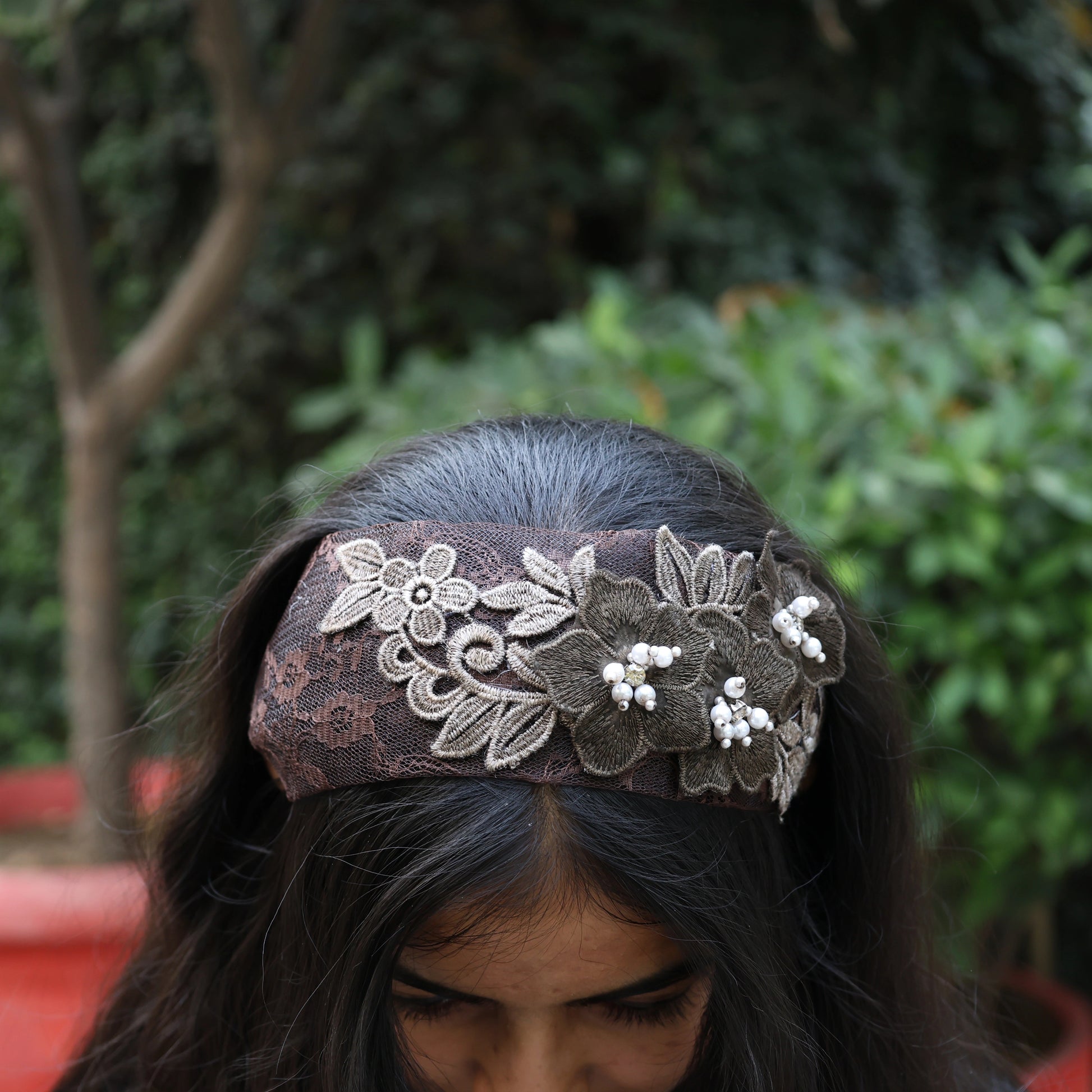 Three flower broad hairbands featuring lace and pearl embellishments worn on dark hair outdoors
