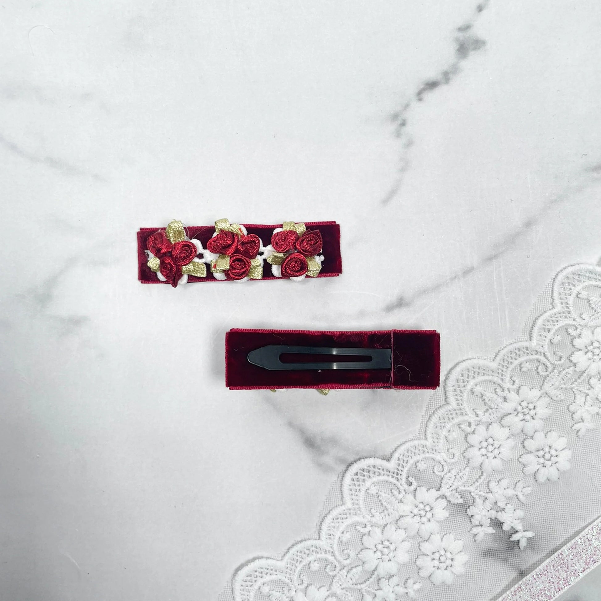 Red velvet flower hair pins adorned with small velvet roses and gold leaves on marble background