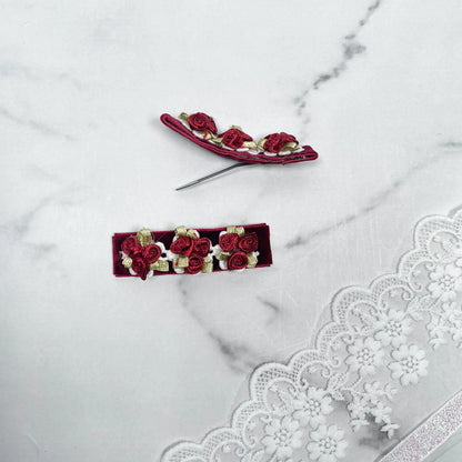 Red velvet flower hair pins with small roses and green leaves on white lace background