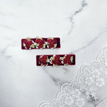 Pair of red velvet flower hair pins with embroidered roses and gold leaves on marble background