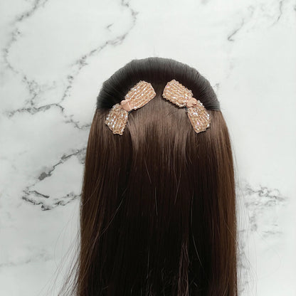 Crystal bow hair pins in light pink attached to dark brown hair on a marble background
