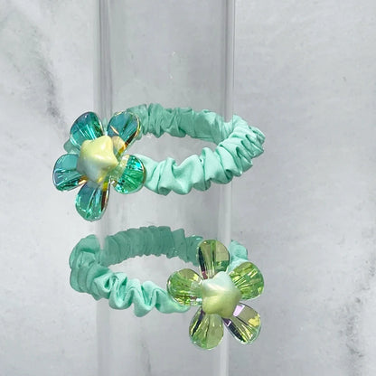Light green shiny daisy flower hair ties with translucent blue and yellow petals on elastic bands