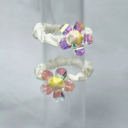 Shiny daisy flower hair ties with iridescent petals and star-shaped centers on white elastic bands