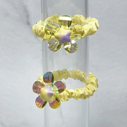 Yellow scrunchie hair ties featuring shiny daisy flower hair ties with iridescent petals and star centers