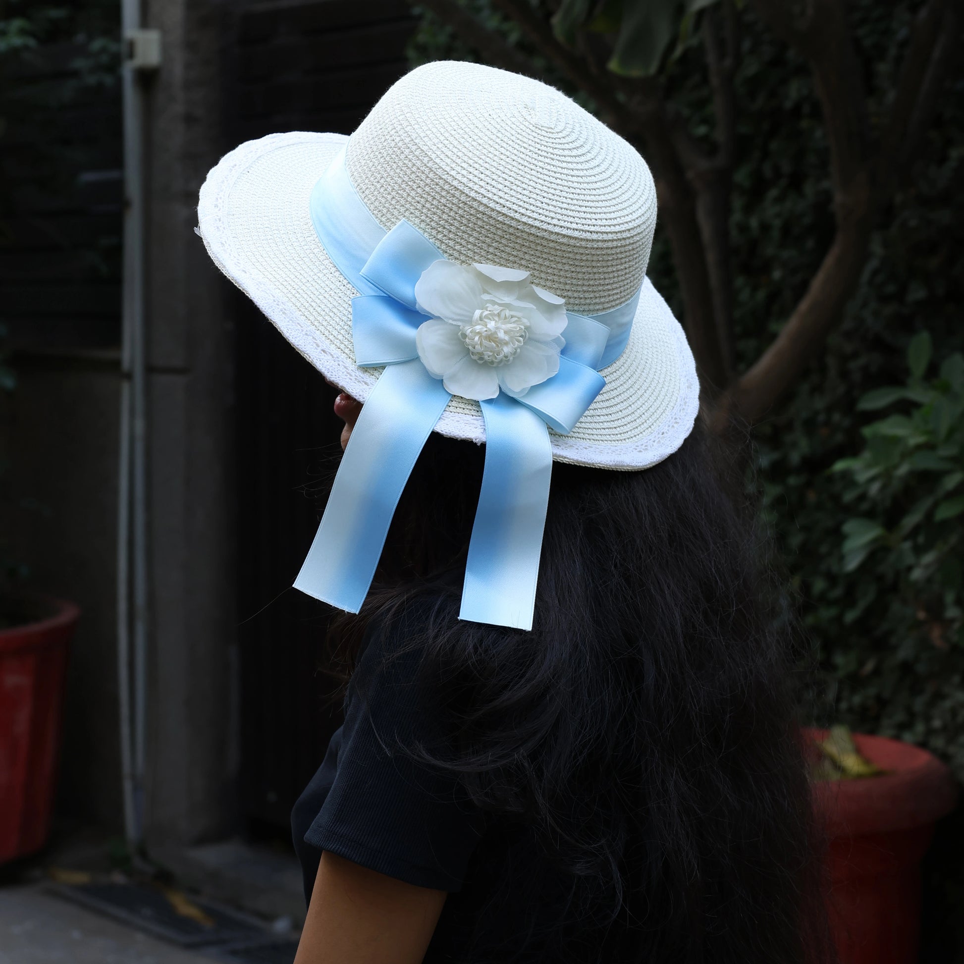 White straw hat with blue ribbon and decorative flower worn by person outdoors